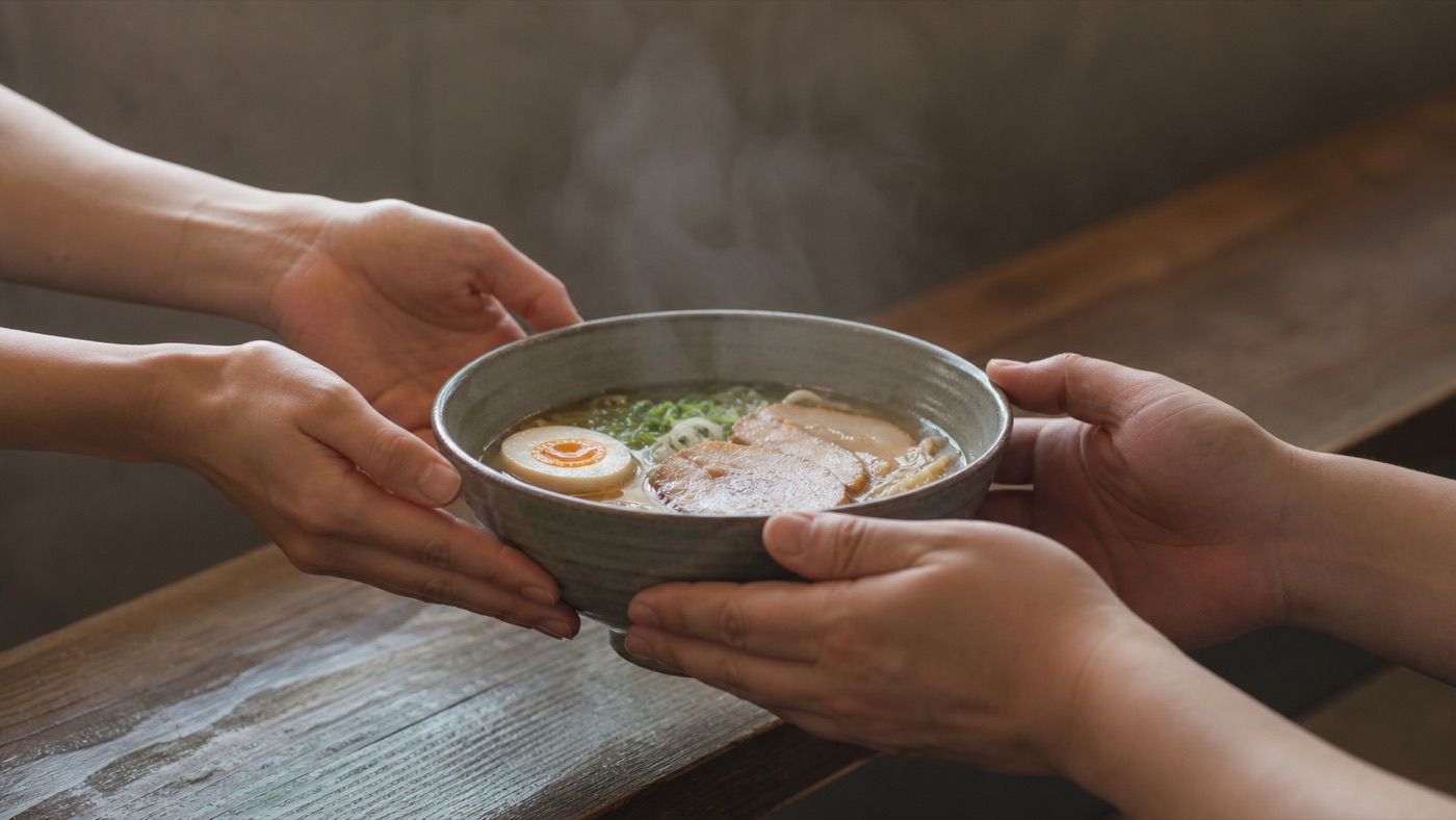 カウンター越しに、湯気の立つ丼を差し出す手と、受け取る手