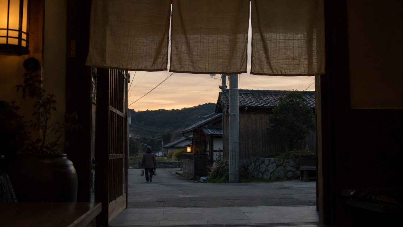 夕方、のれんの内側からお客さんを見送る後ろ姿